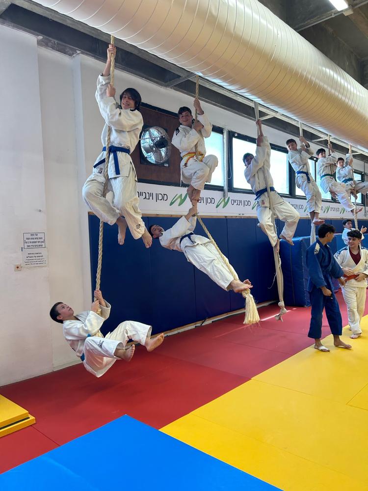 ילדים בחליפות ג׳ודו מטפסים על חבלים באולם האימונים